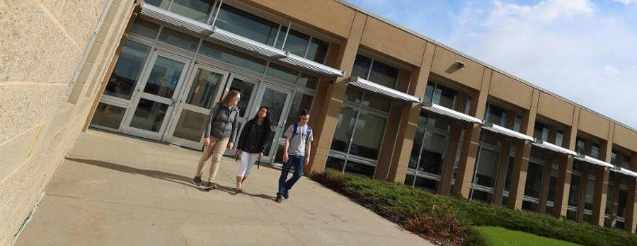Three students walking on sidewalk in sunshine by health building